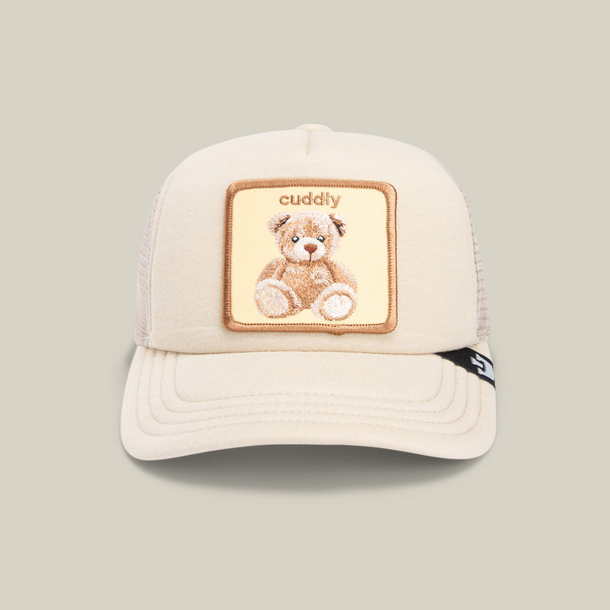 The Goorin Bros. Cuddle Time is a beige kids’ trucker hat with a mesh back, featuring a teddy bear patch and “cuddly” embroidered above—a cute and cozy cap for any child.