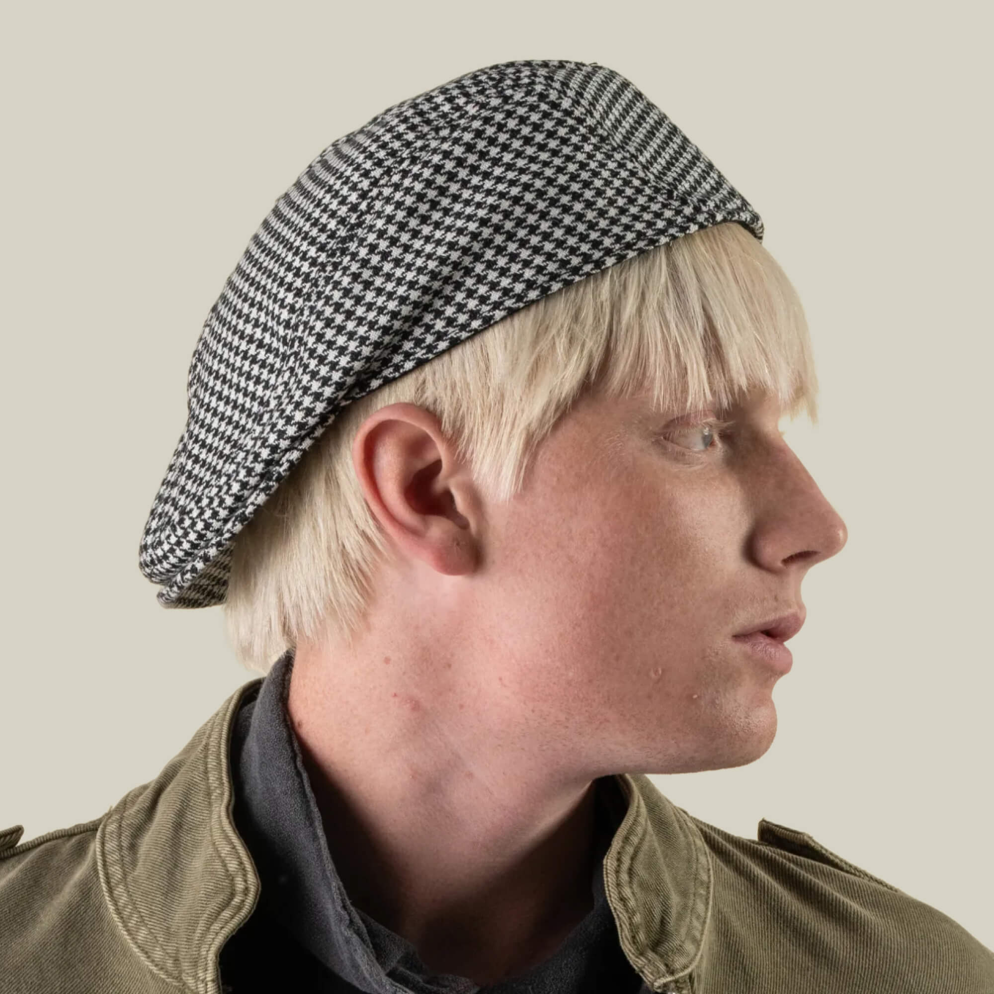 A person with blond hair is shown in profile against a plain background, wearing the Norwood houndstooth-patterned wool beret by Goorin Bros. and a green jacket.