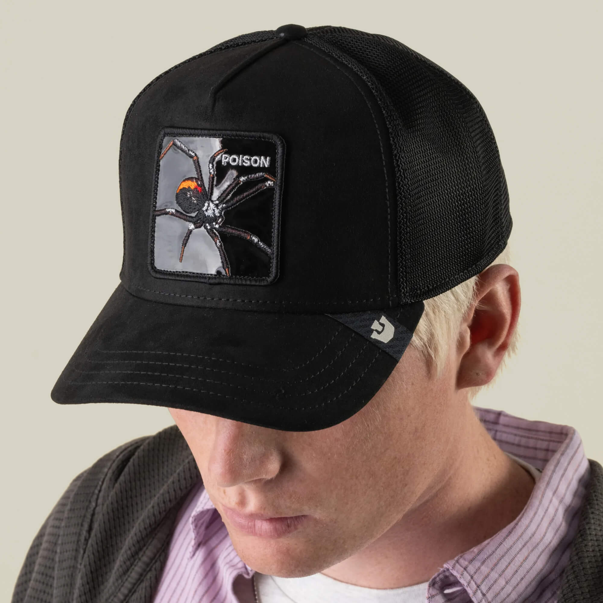 A person wearing the Goorin Bros. Black Out Spider hat, featuring an embroidered spider patch with the word “POISON,” channels serious blackout spider energy while looking downward.
