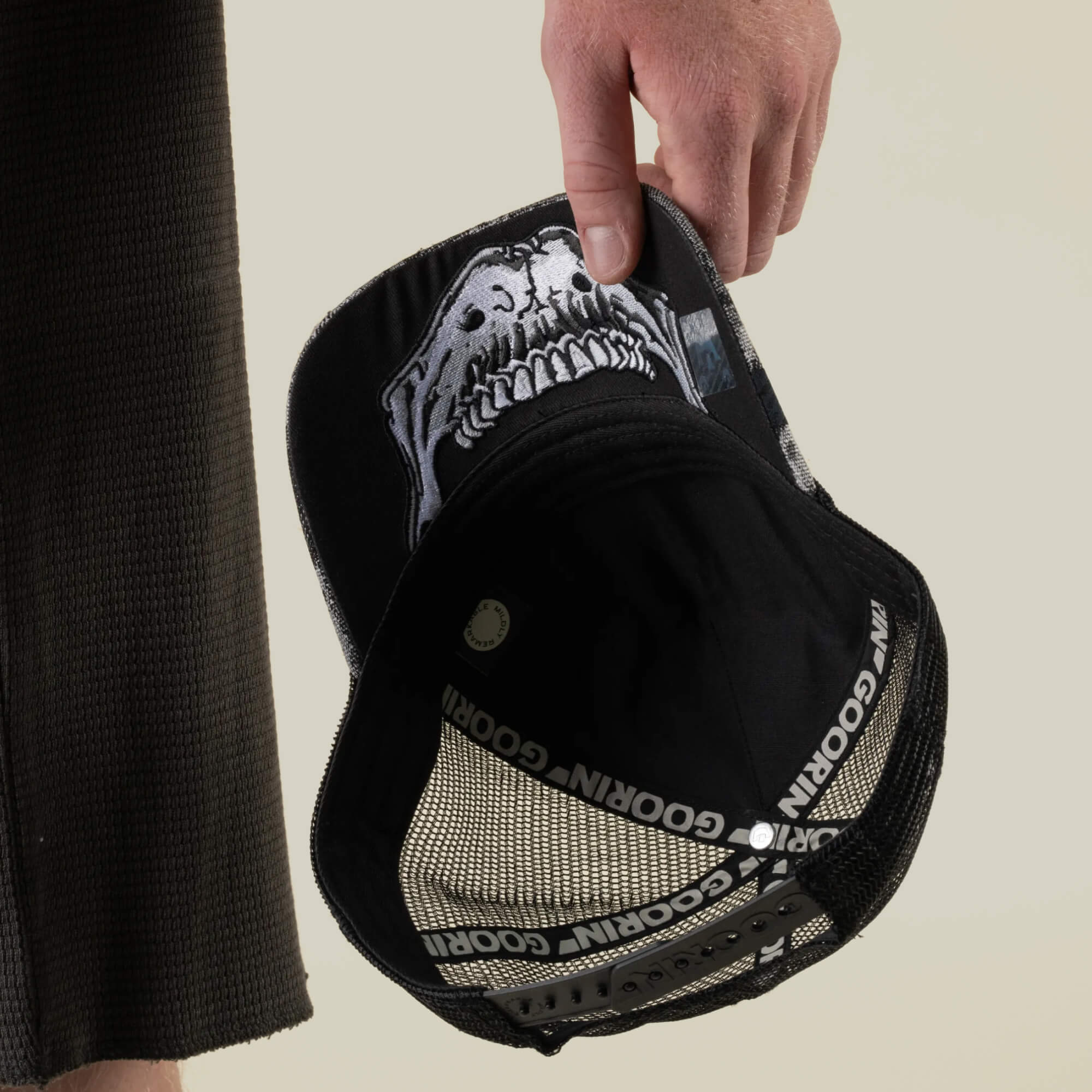 A person holds the Bone Head Unalive trucker hat by Goorin Bros., featuring a black and white skull design, a breathable mesh back, and distinctive Goorin Bros. branding inside.