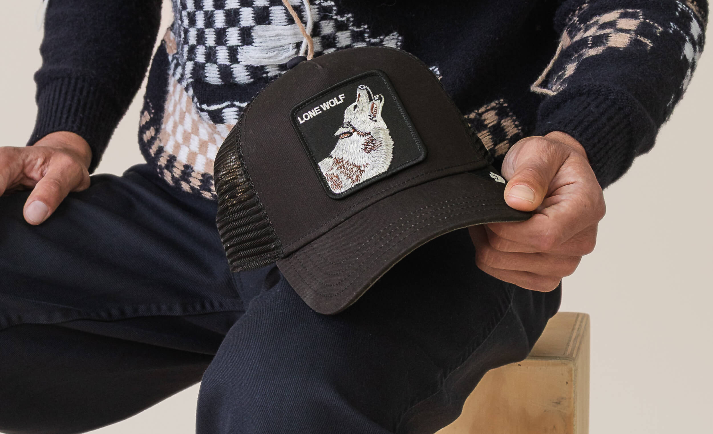 Person holding a black cap with a rabbit patch and 'Long Wolf' branding.