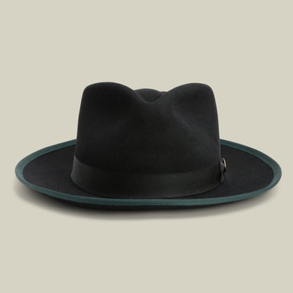 River Gray by Goorin Bros. is a black wide brim fedora crafted from premium merino wool, featuring a dark green edge trim and a black ribbon band. Set against a plain beige background, this American-made hat offers timeless style with exceptional craftsmanship.