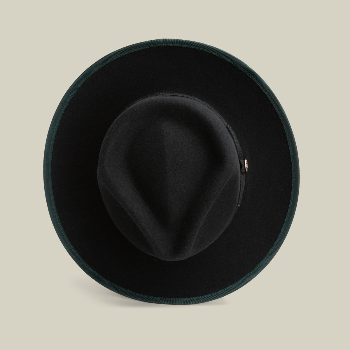 River Gray by Goorin Bros. is an American-made merino wool fedora in black felt, featuring a wide brim viewed from above, a creased crown, and a dark green trim around the edge, set against a beige background. This hat combines timeless style with quality craftsmanship.