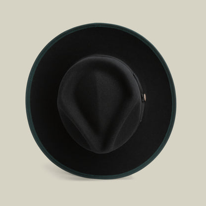 River Gray by Goorin Bros. is an American-made merino wool fedora in black felt, featuring a wide brim viewed from above, a creased crown, and a dark green trim around the edge, set against a beige background. This hat combines timeless style with quality craftsmanship.