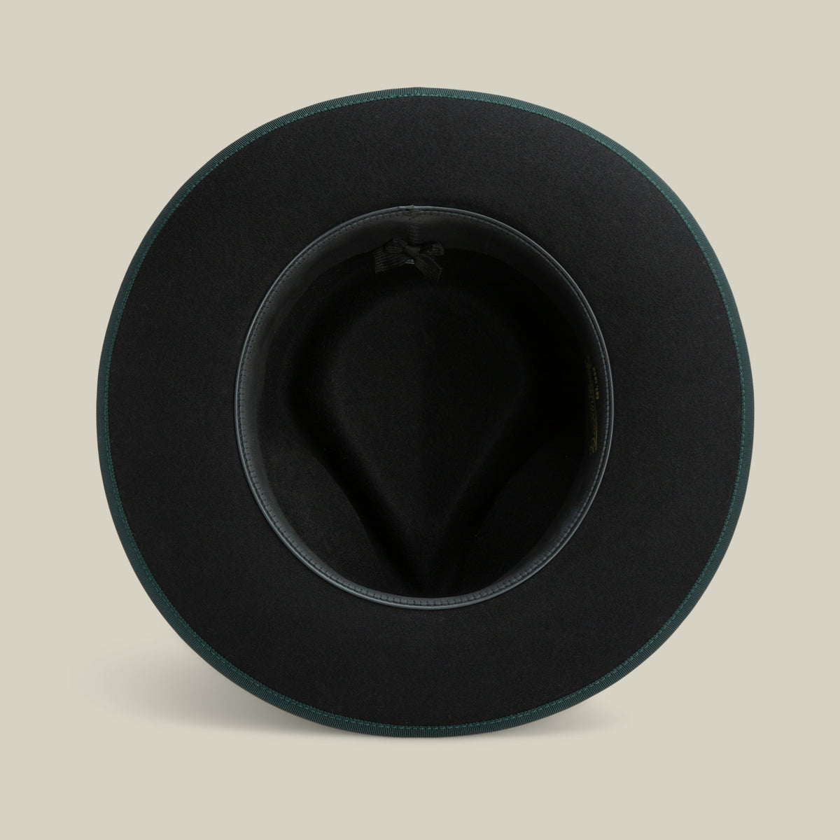 Top-down view of the “River Gray” fedora by Goorin Bros., an American-made black merino wool hat with a wide brim, featuring a dark inner band and a small bow, displayed on a neutral beige background.