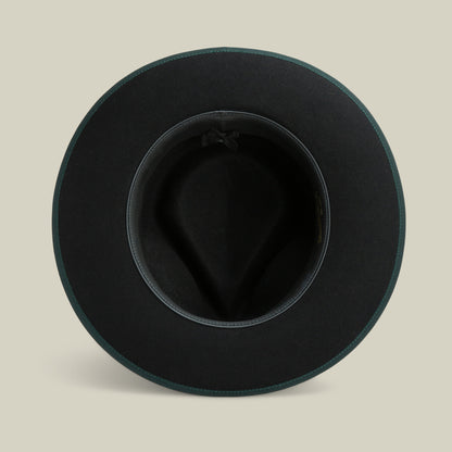 Top-down view of the “River Gray” fedora by Goorin Bros., an American-made black merino wool hat with a wide brim, featuring a dark inner band and a small bow, displayed on a neutral beige background.