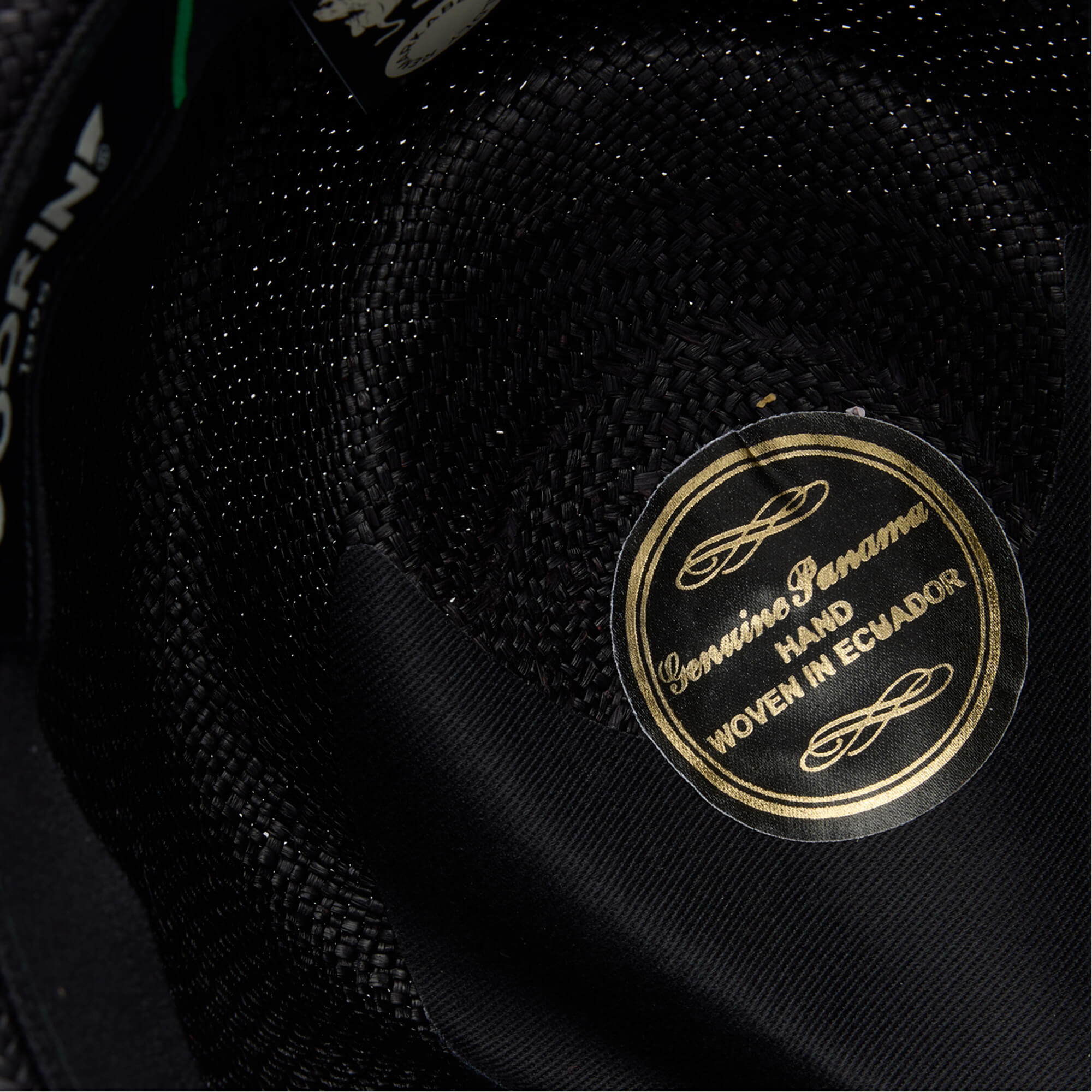 Close-up of the inside of a John Sr. black toquilla teardrop fedora by Goorin Bros., featuring a gold label reading Genuine Panama Hand Woven in Ecuador and offering 50 UPF sun protection.