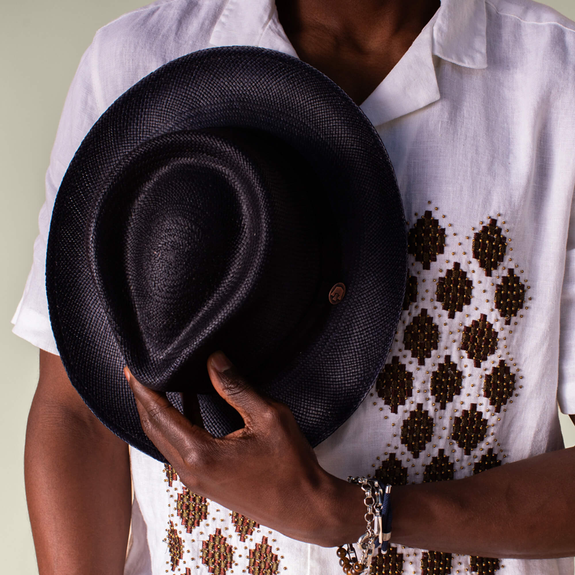 A person in a white patterned shirt holds the Goorin Bros. John Sr. black toquilla fedora (50 UPF) in front of their chest.