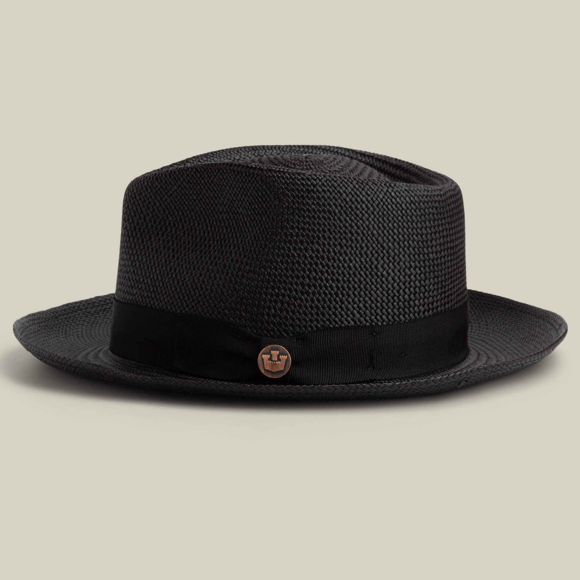 The John Sr. by Goorin Bros. is a black toquilla teardrop fedora with a black band, round metallic side emblem, and 50 UPF sun protection, shown on a plain beige background.