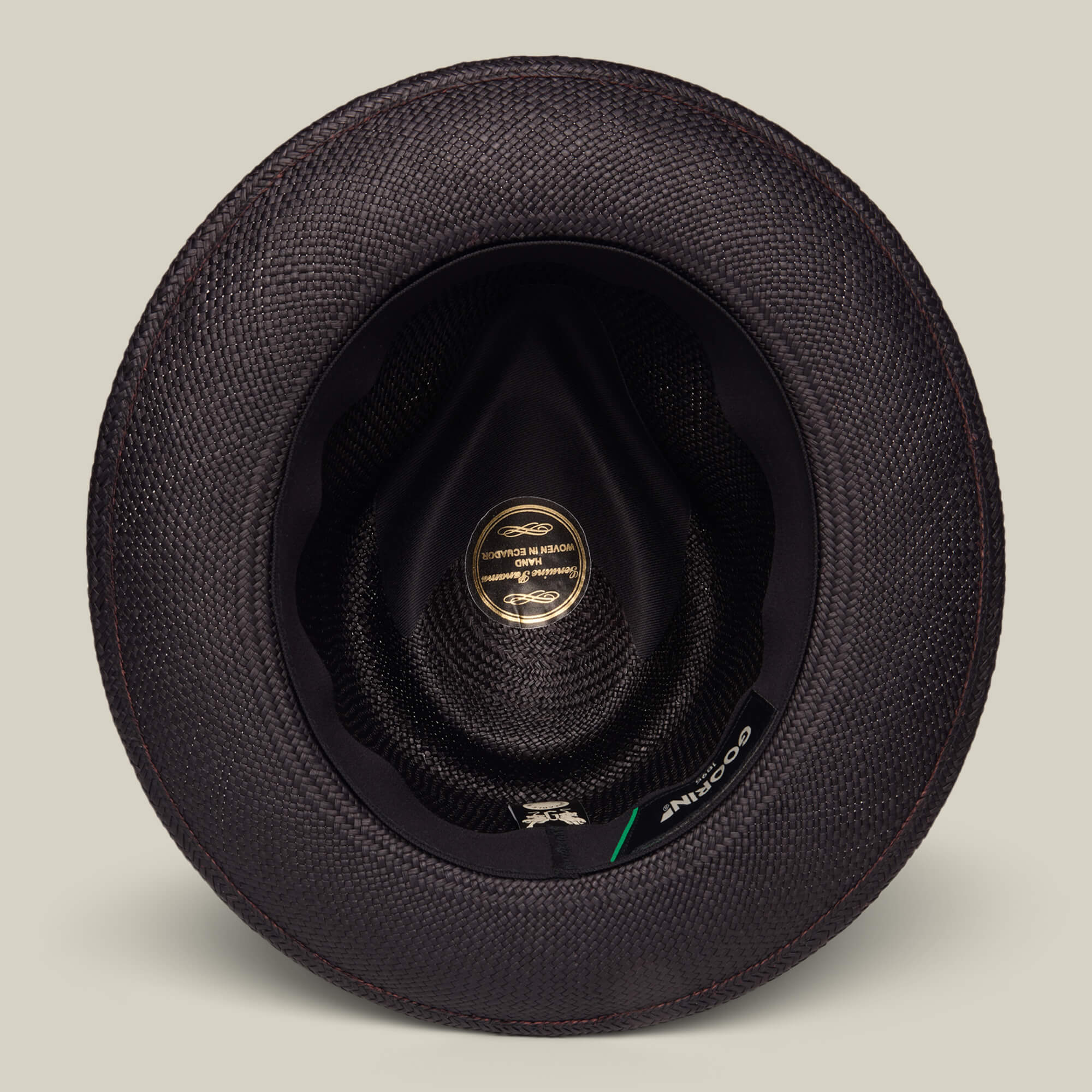 Top-down view of the inside of a black textured John Sr. teardrop fedora by Goorin Bros., featuring a gold label, black inner lining, and designed for 50 UPF sun protection.