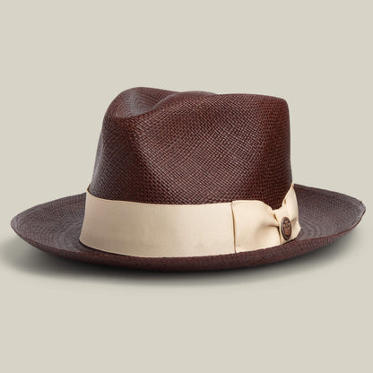 The John Sr. by Goorin Bros. is a brown toquilla teardrop fedora with a wide, light beige ribbon and decorative bow, offers 50 UPF sun protection, and is shown on a neutral background.