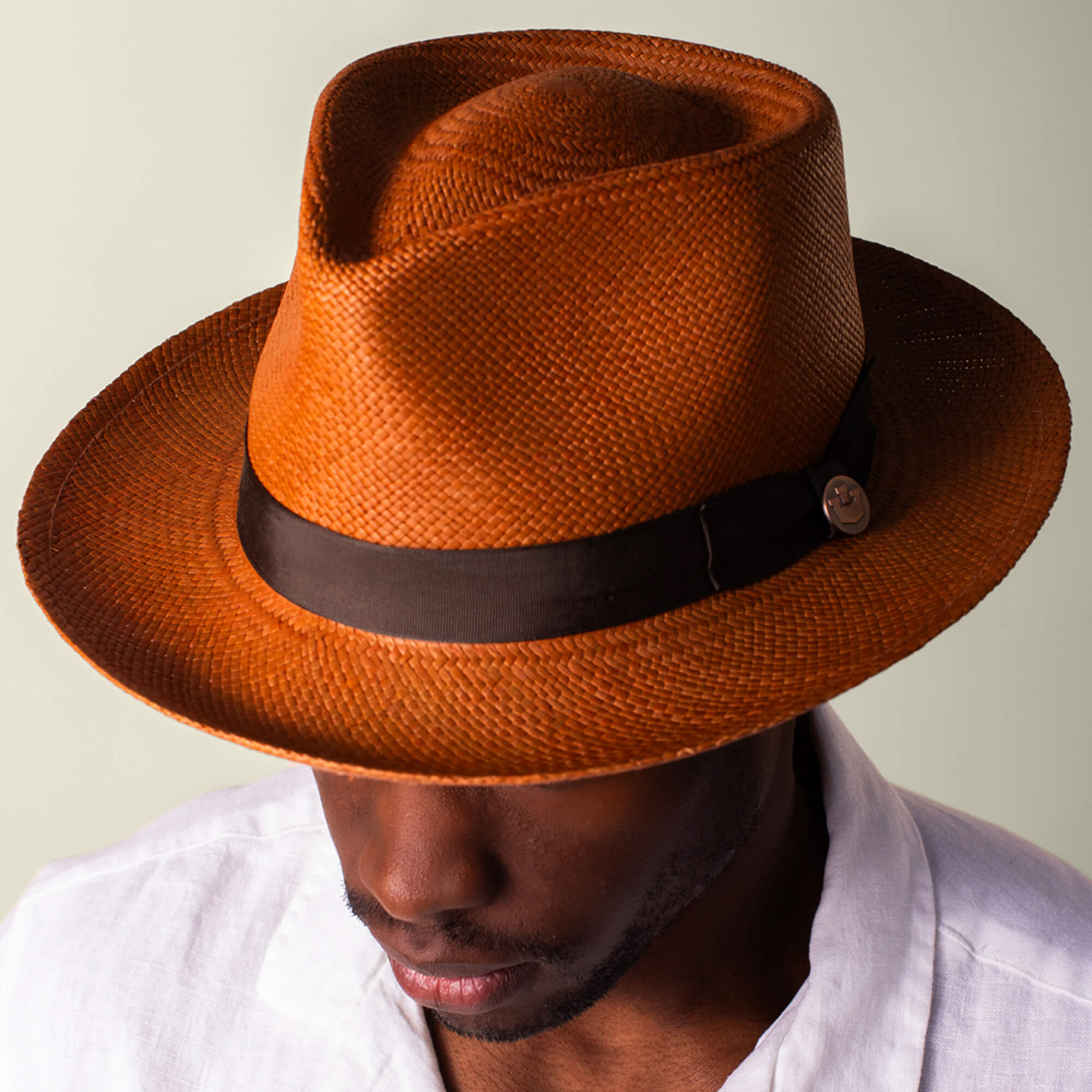 A man in a Goorin Bros. John Sr. brown toquilla fedora with dark band (50 UPF sun protection) and a white shirt looks downward against a neutral background.