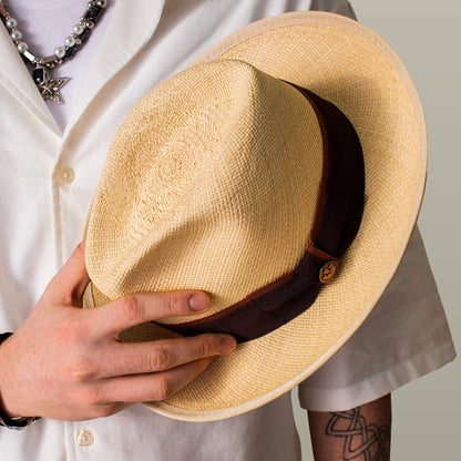 A person wearing a white shirt and jewelry holds the Goorin Bros. Hartman beige straw fedora with a dark brown grosgrain band.