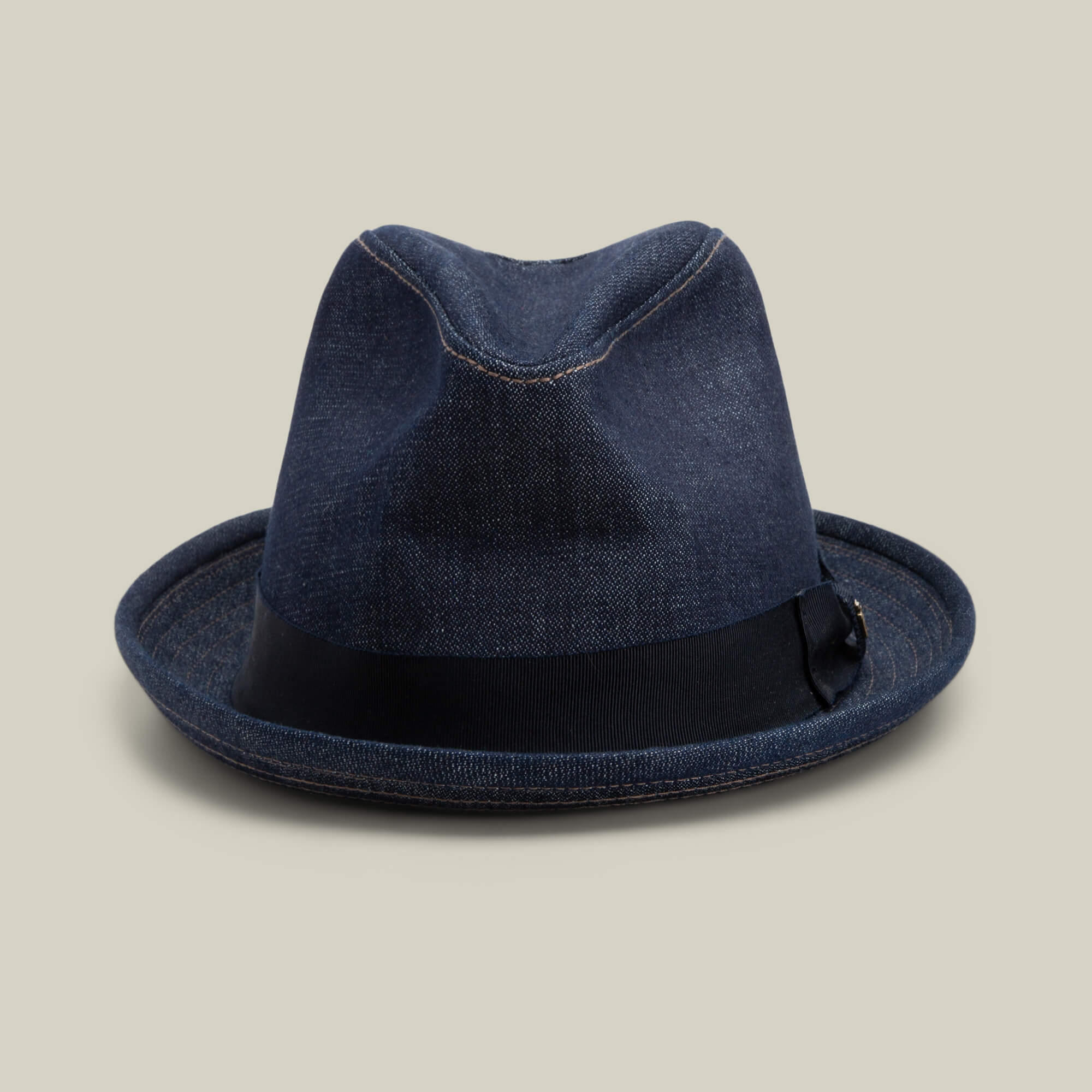 The Goorin Bros. Noisy Big Stepper fedora in indigo denim features a sharp crown and black ribbon band, showcased on a plain light beige background.