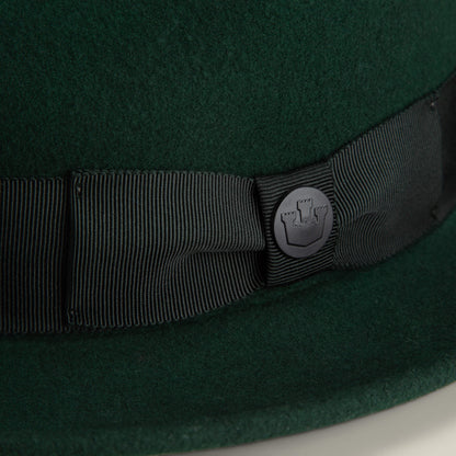 Close-up of Dean the Butcher by Goorin Bros.—a dark green felt fedora with a black grosgrain ribbon and round metal castle emblem, American-made for all seasons.