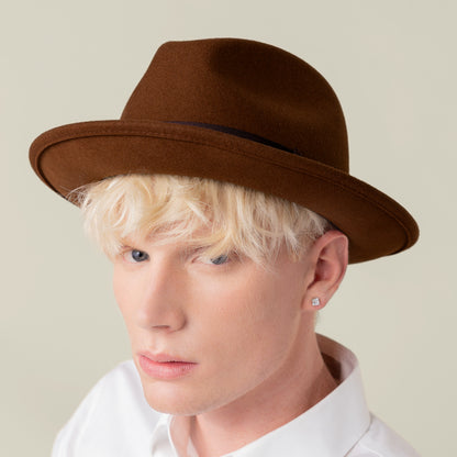 A light blonde person wears the Goorin Bros. "Dean the Butcher" brown fedora, a white shirt, and a square stud earring, looking at the camera against a neutral background.