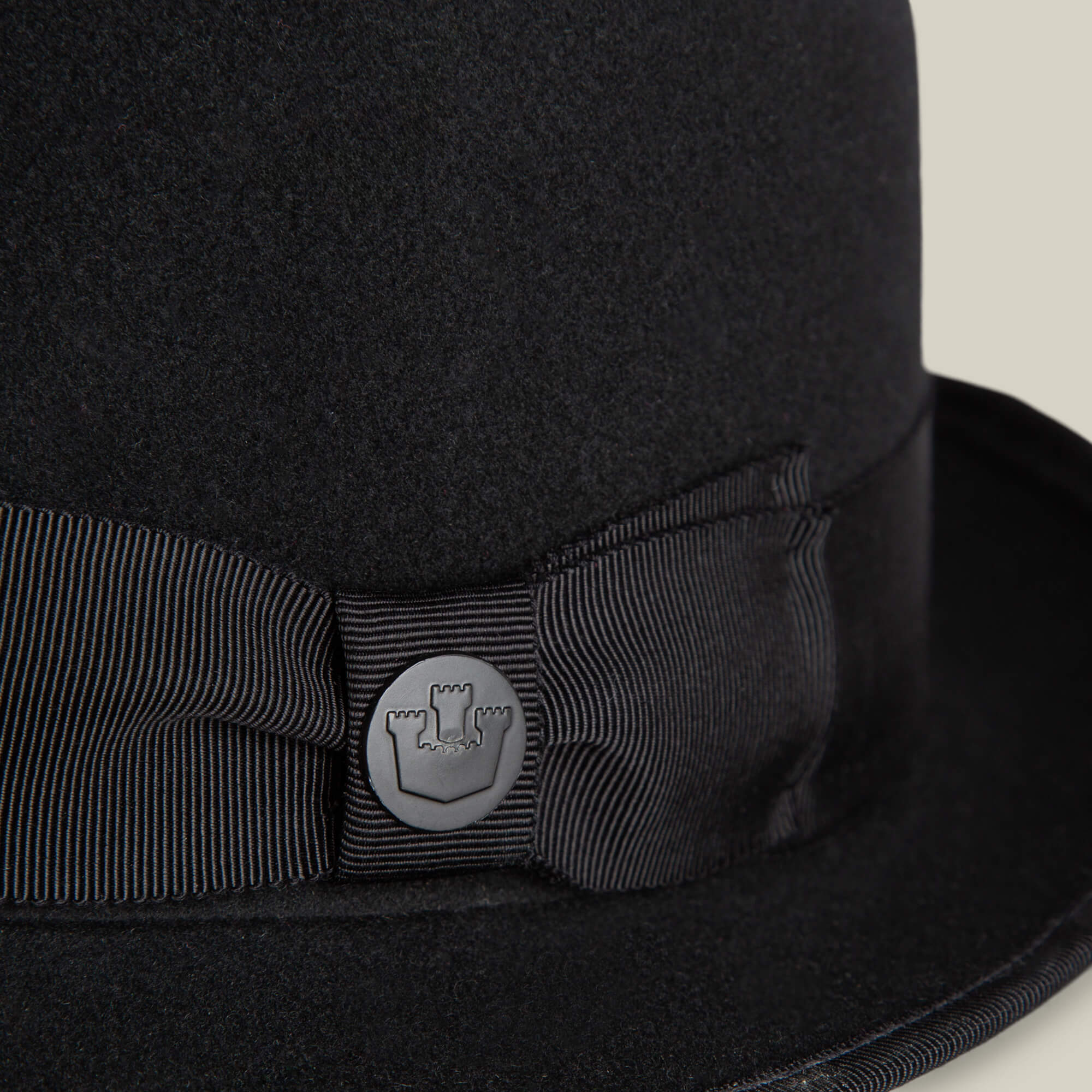 Close-up of the Slick Carter by Goorin Bros.: a black felt hat with a ribbon and round metal pin featuring a castle turret emblem, showcasing effortless style and a classic wool short brim design.