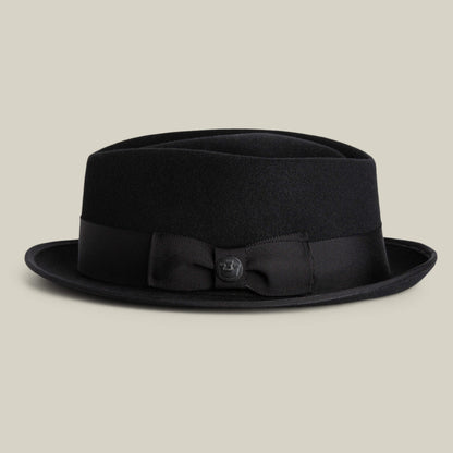 The Goorin Bros. Slick Carter is a black wool pork pie hat with a flat crown, short brim, and black ribbon band detailed with a bow and button—ideal for adding stylish flair to any look.