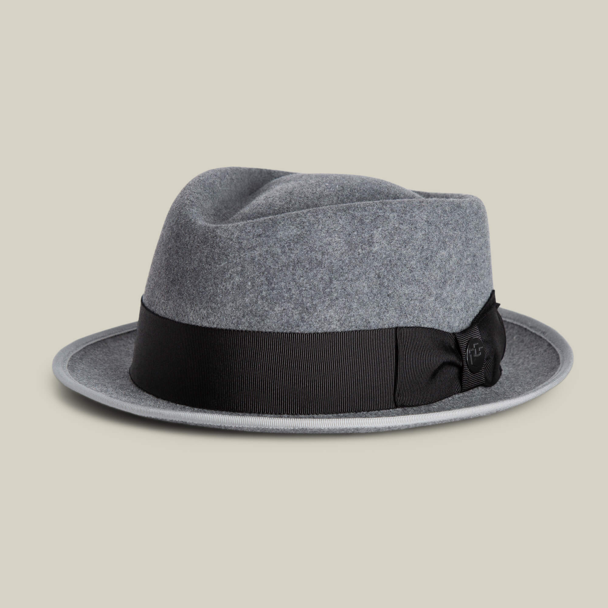 The Slick Carter by Goorin Bros. is a grey felt fedora featuring a black grosgrain ribbon band and bow, plus a wool short brim. Displayed on a neutral background, it brings effortless style and timeless elegance to any look.