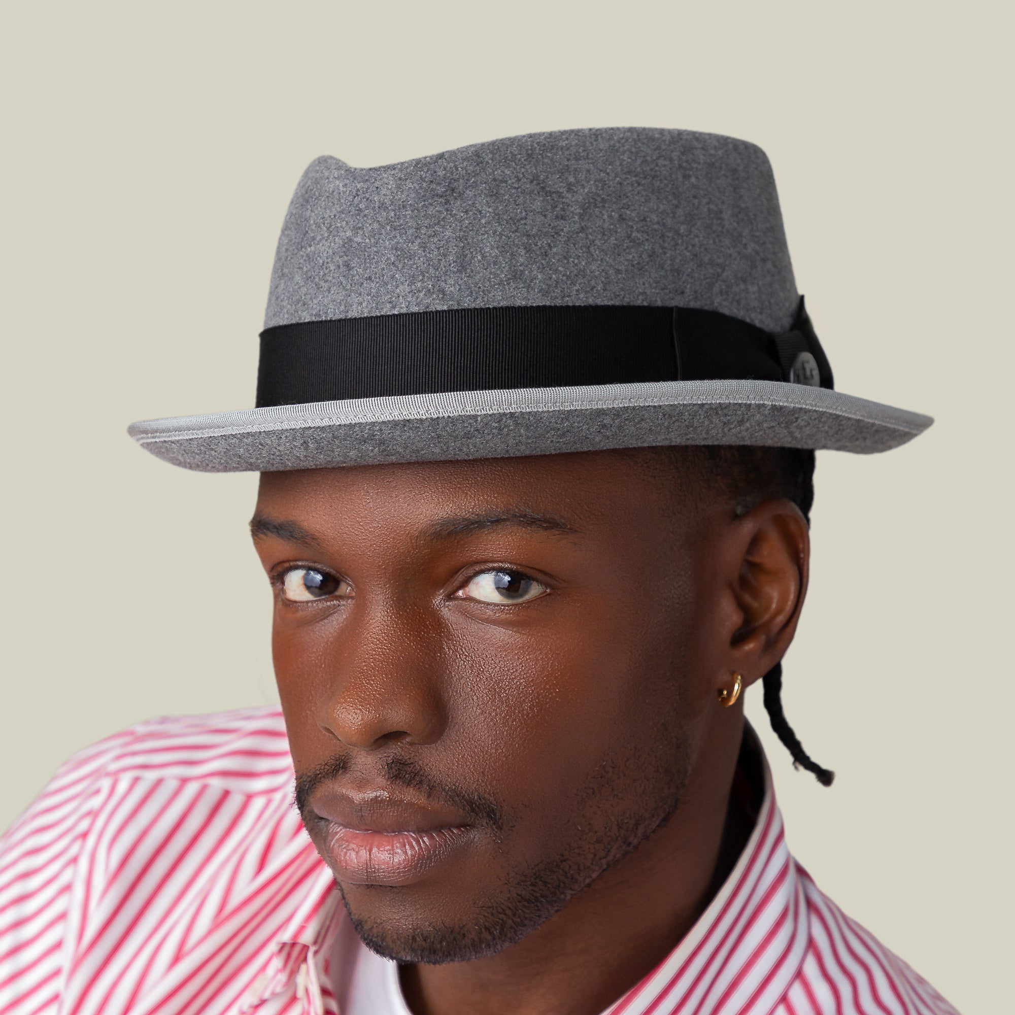 A man exudes effortless style in the Slick Carter gray wool short brim fedora by Goorin Bros. and a red-and-white striped shirt, looking at the camera against a plain background.