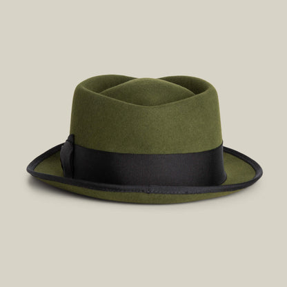 The Goorin Bros. Slick Carter is an olive green wool pork pie hat with a short, upturned brim and black ribbon band, shown on a beige background. This stylish piece adds charm to any outfit.