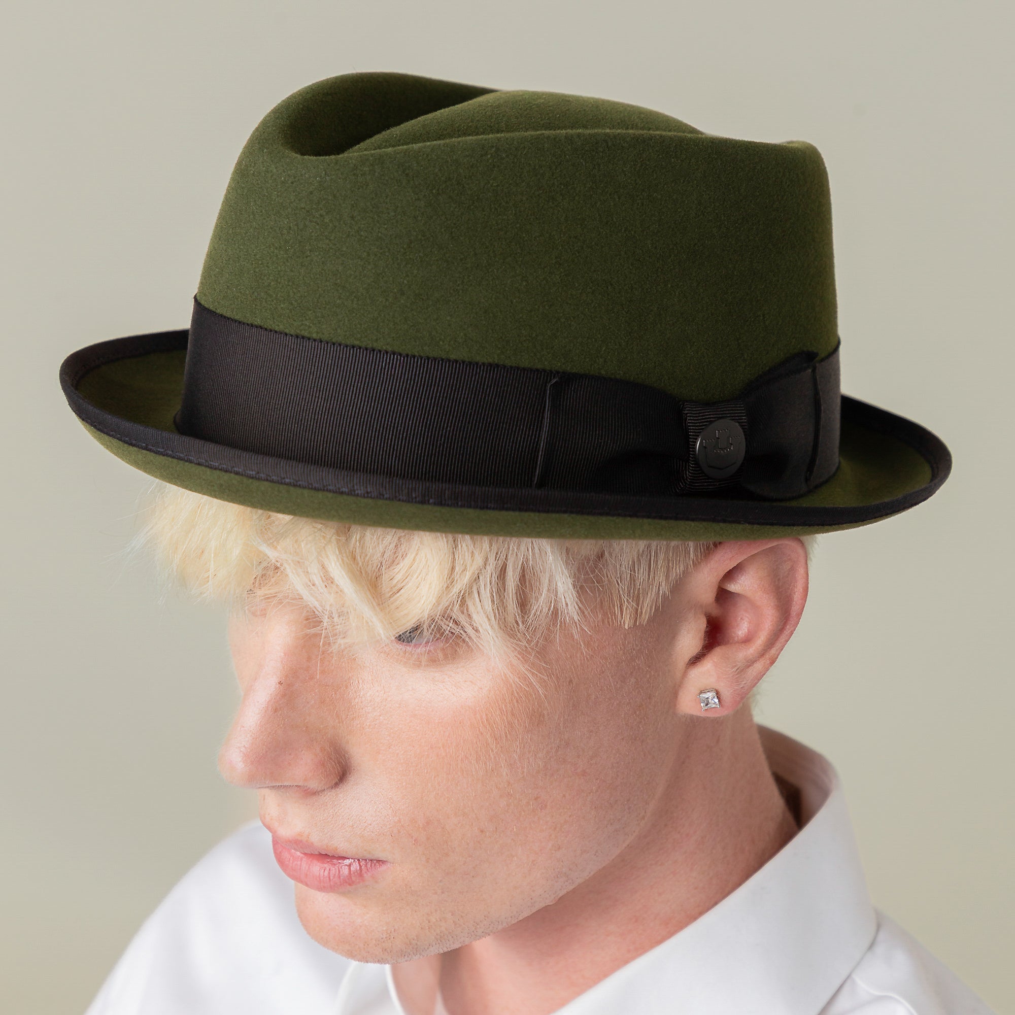 A person with light blonde hair wears the Goorin Bros. Slick Carter green wool short brim trilby with a black ribbon and a white collared shirt, channeling effortless style while facing slightly downward.