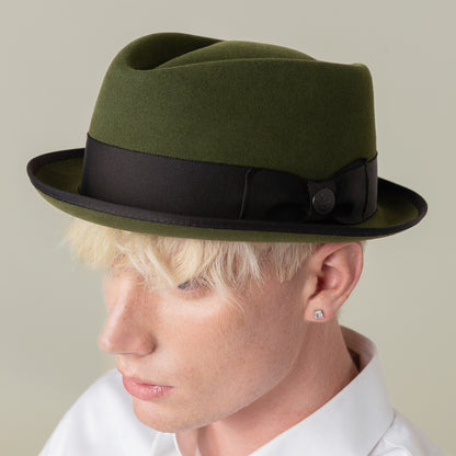 A person with light blonde hair wears the Goorin Bros. Slick Carter green wool short brim trilby with a black ribbon and a white collared shirt, channeling effortless style while facing slightly downward.