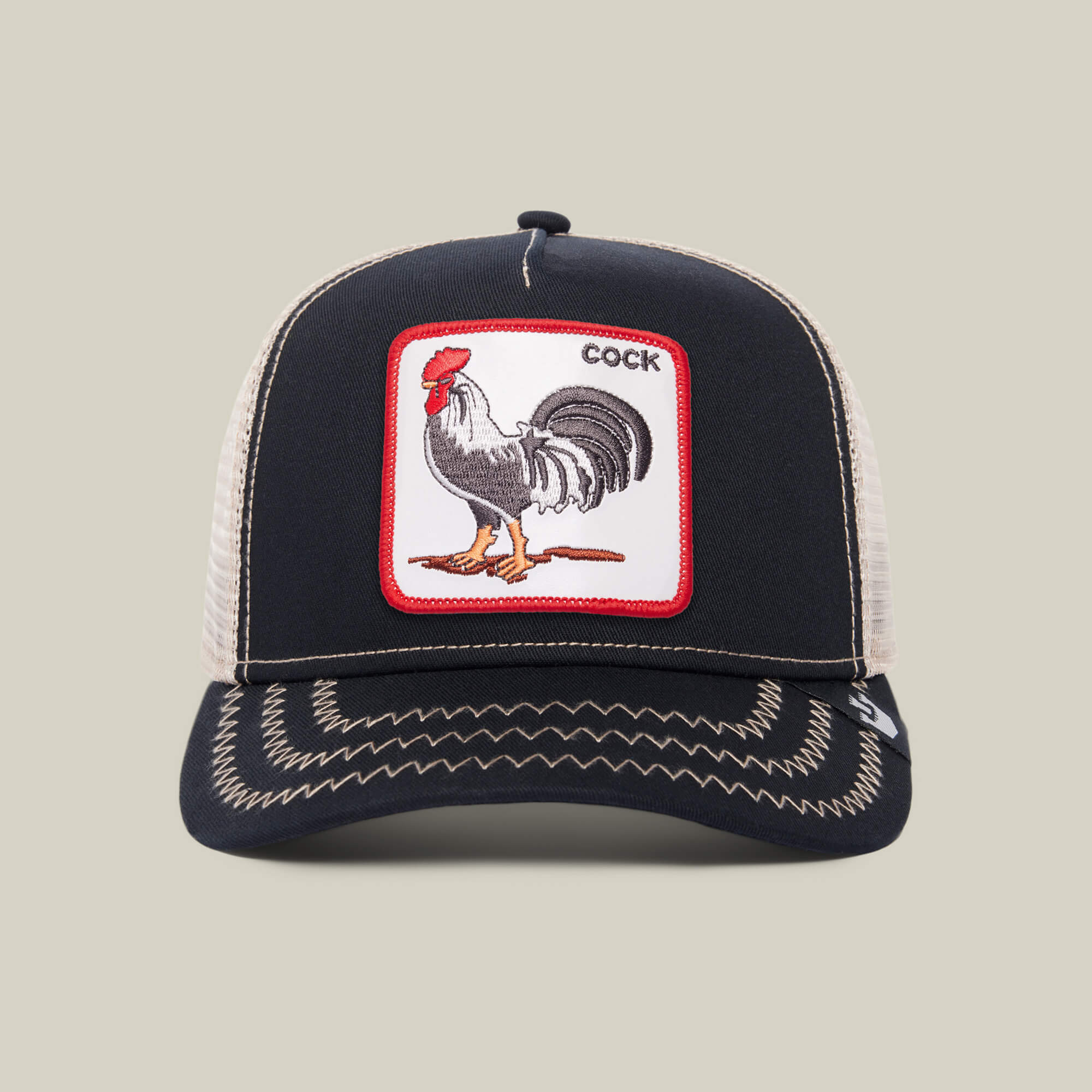 The Farm’s "The Cock" is a black and beige trucker hat with a front patch showing a rooster illustration and the word COCK in the top right corner.