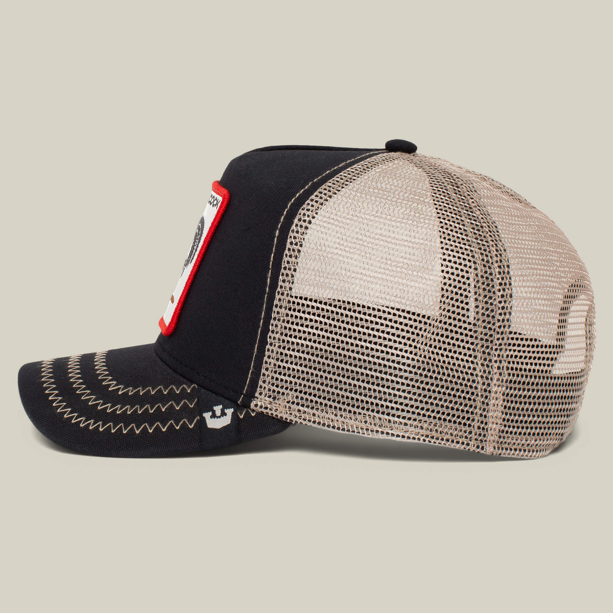 The Farm's "The Cock" is a black and beige mesh trucker hat with white stitching and a front rectangular patch featuring a side-profile rooster on a plain background.