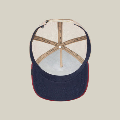 The underside of The Farm's "The Cock" trucker hat—navy blue brim, red edge, beige mesh panels, and tan seams labeled THE FARM—subtly nods to the rooster, a classic resurrection symbol.