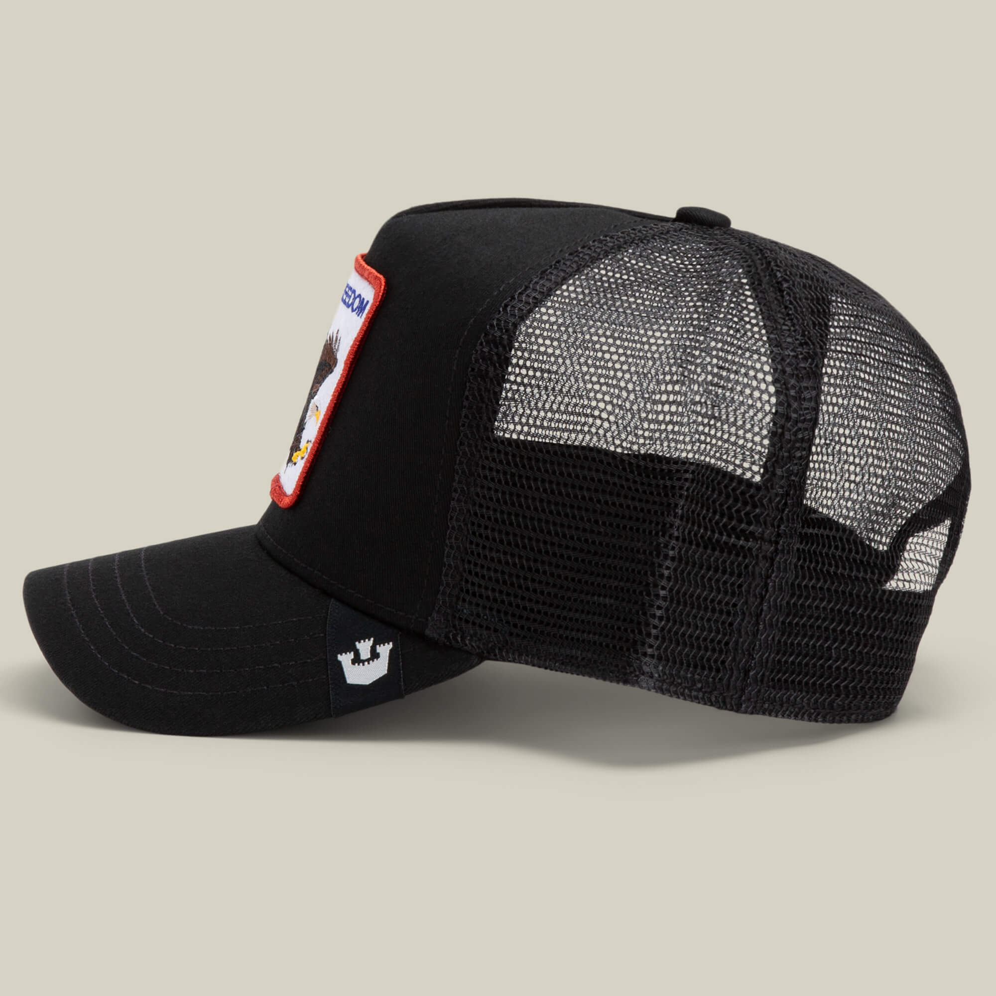 The Farm’s The Freedom Eagle is a black mesh trucker hat with a curved bill, side crown logo patch, and a front patch with red border and eagle art—reminding you to keep your distance in style.