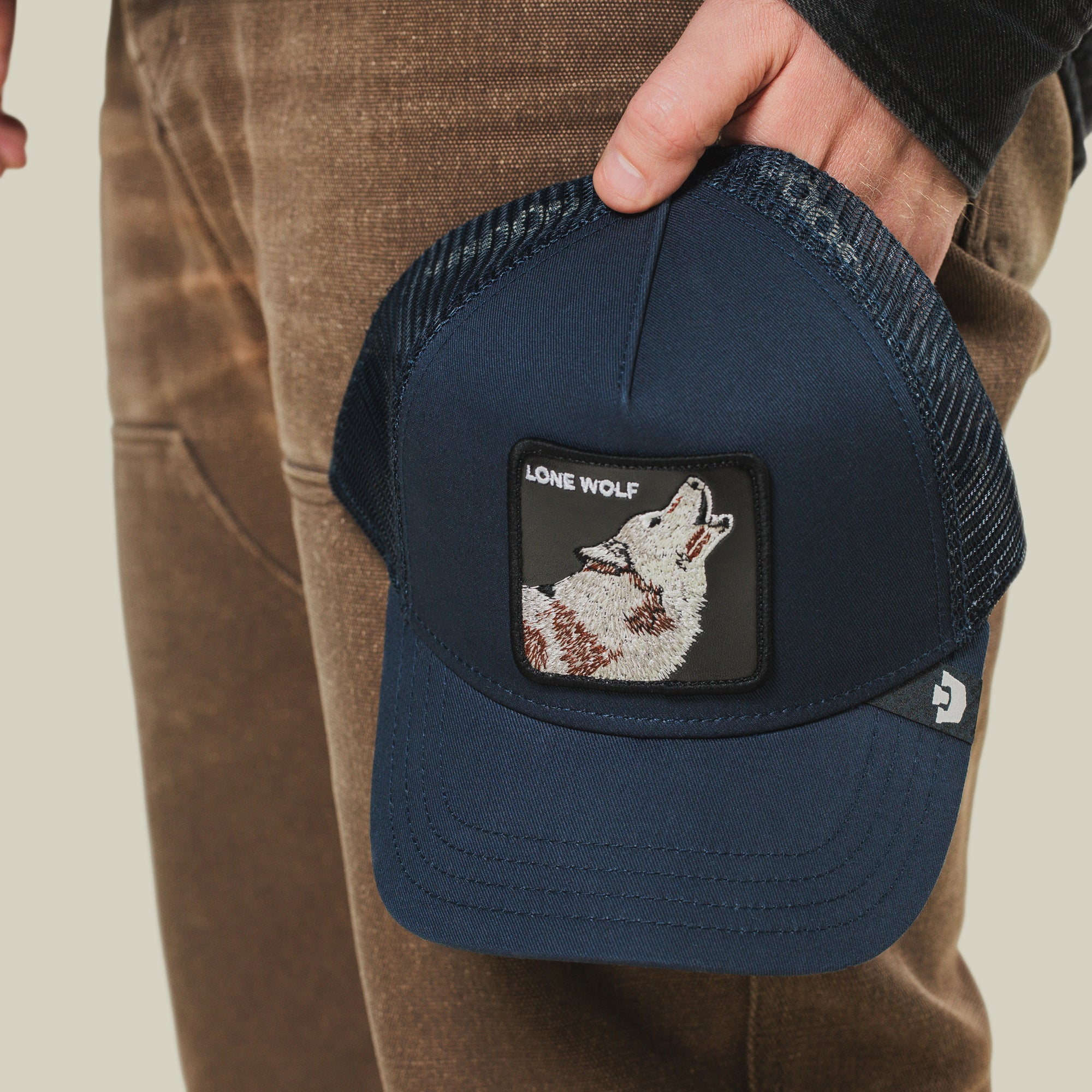 A person holds The Farm’s "The Lone Wolf" navy mesh trucker hat, featuring a patch with a howling wolf and text “Lone Wolf”—ideal for independent, anti-conformist spirits.