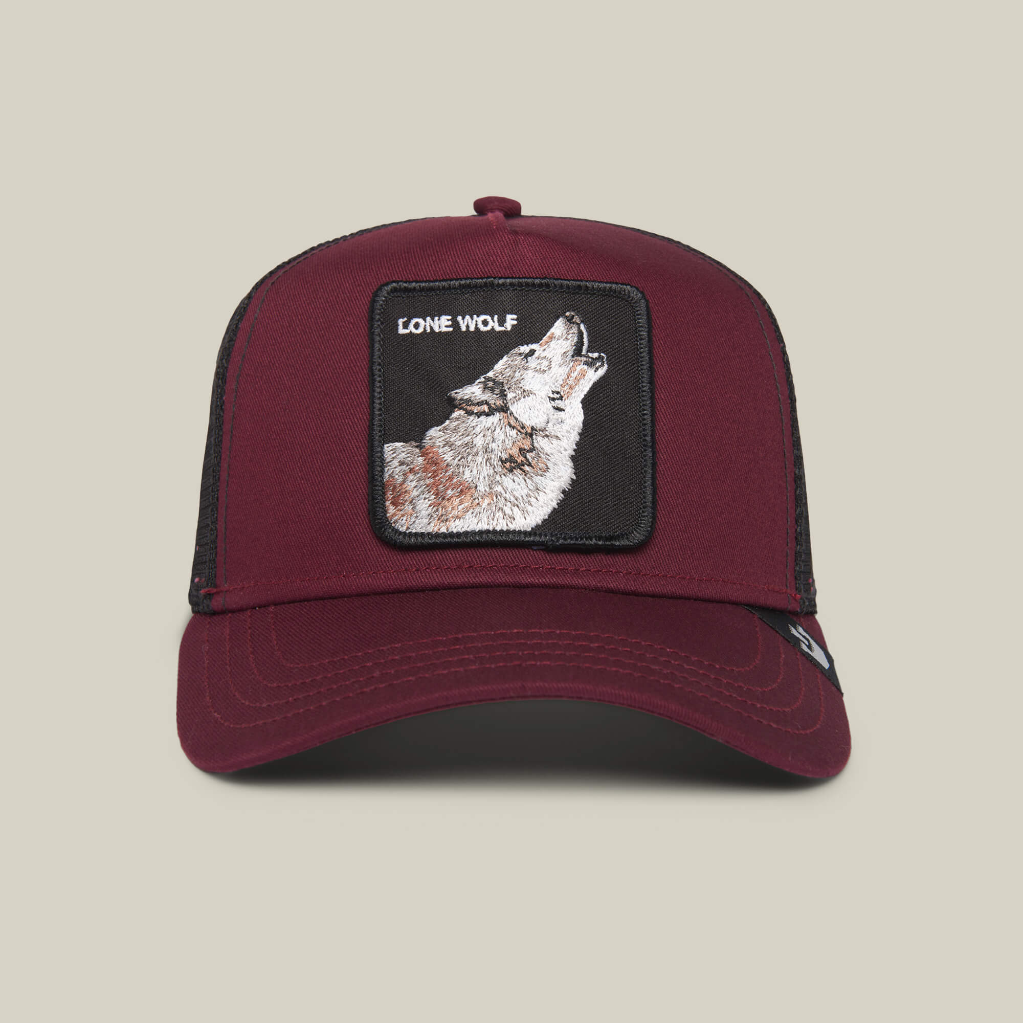 The Farm’s “The Lone Wolf” maroon trucker hat features a black mesh back and a front patch with a howling wolf and LONE WOLF text—ideal for the independent spirit.