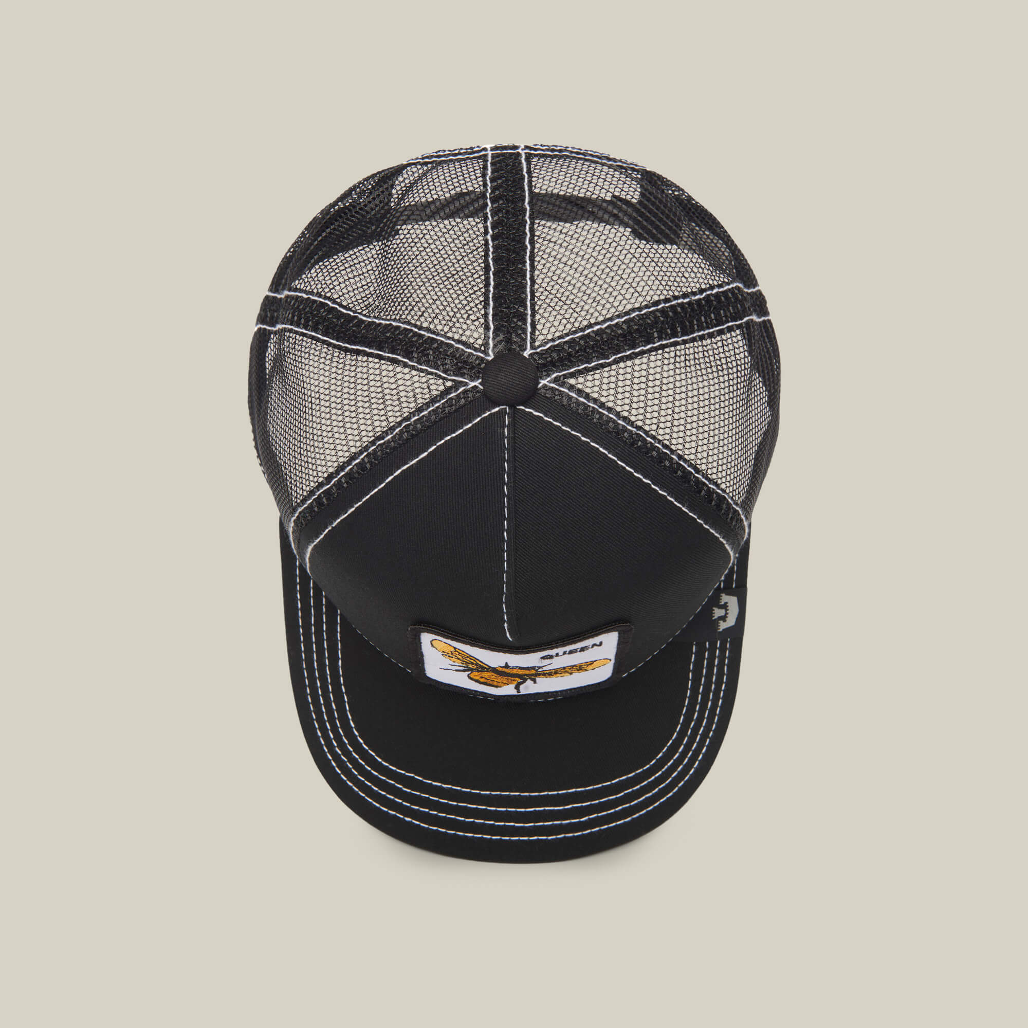 The Queen Bee by The Farm is a black mesh trucker hat with white stitching and a front rectangular embroidered patch featuring a bird graphic—a standout accessory for every look.
