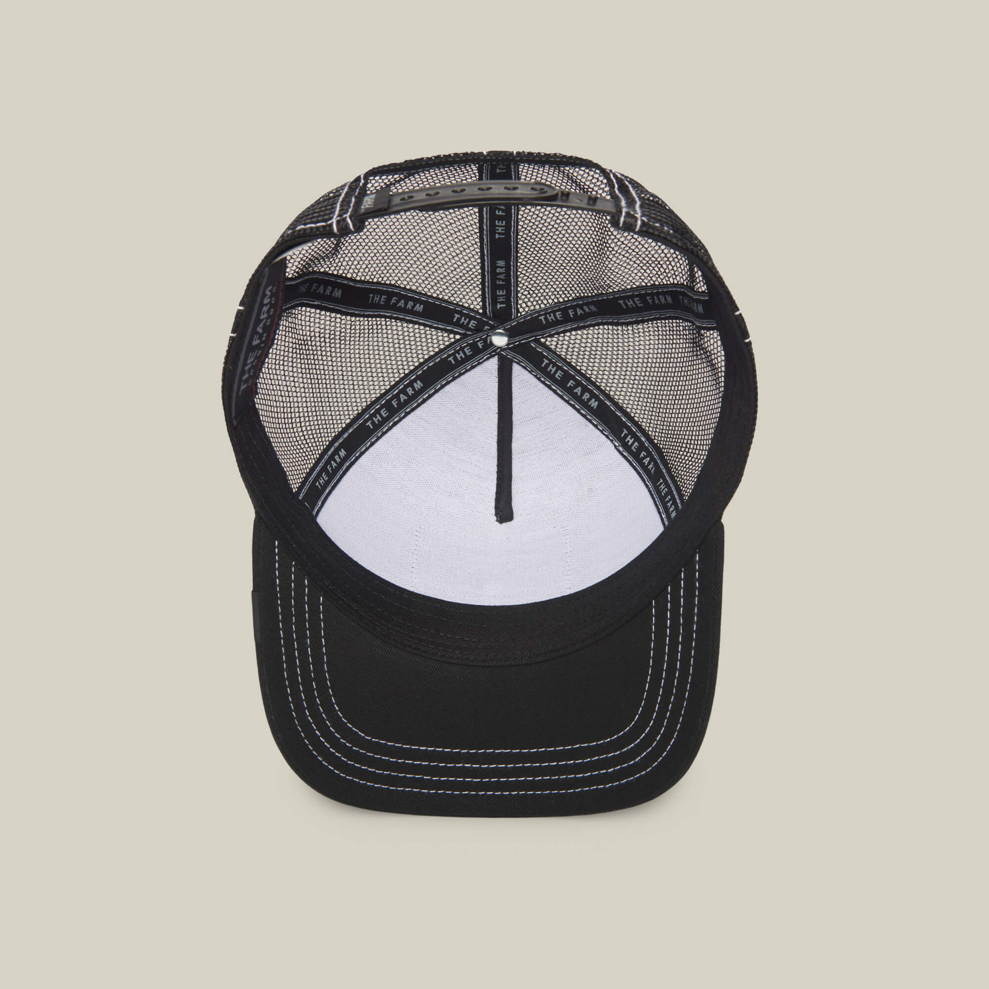 The Queen Bee by The Farm: a black mesh trucker hat with white stitching, inner band featuring THE FARM text, and a white front panel—crafted for those who rule style with confidence.