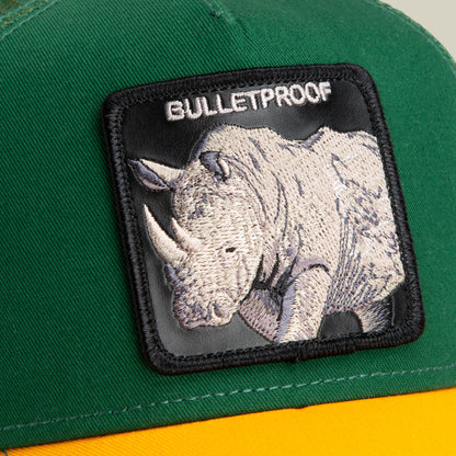 Close-up of The Farm's "The Bulletproof Rhino" cap in green and yellow, featuring a stitched rhinoceros patch and BULLETPROOF text. Please note: All sales are final.