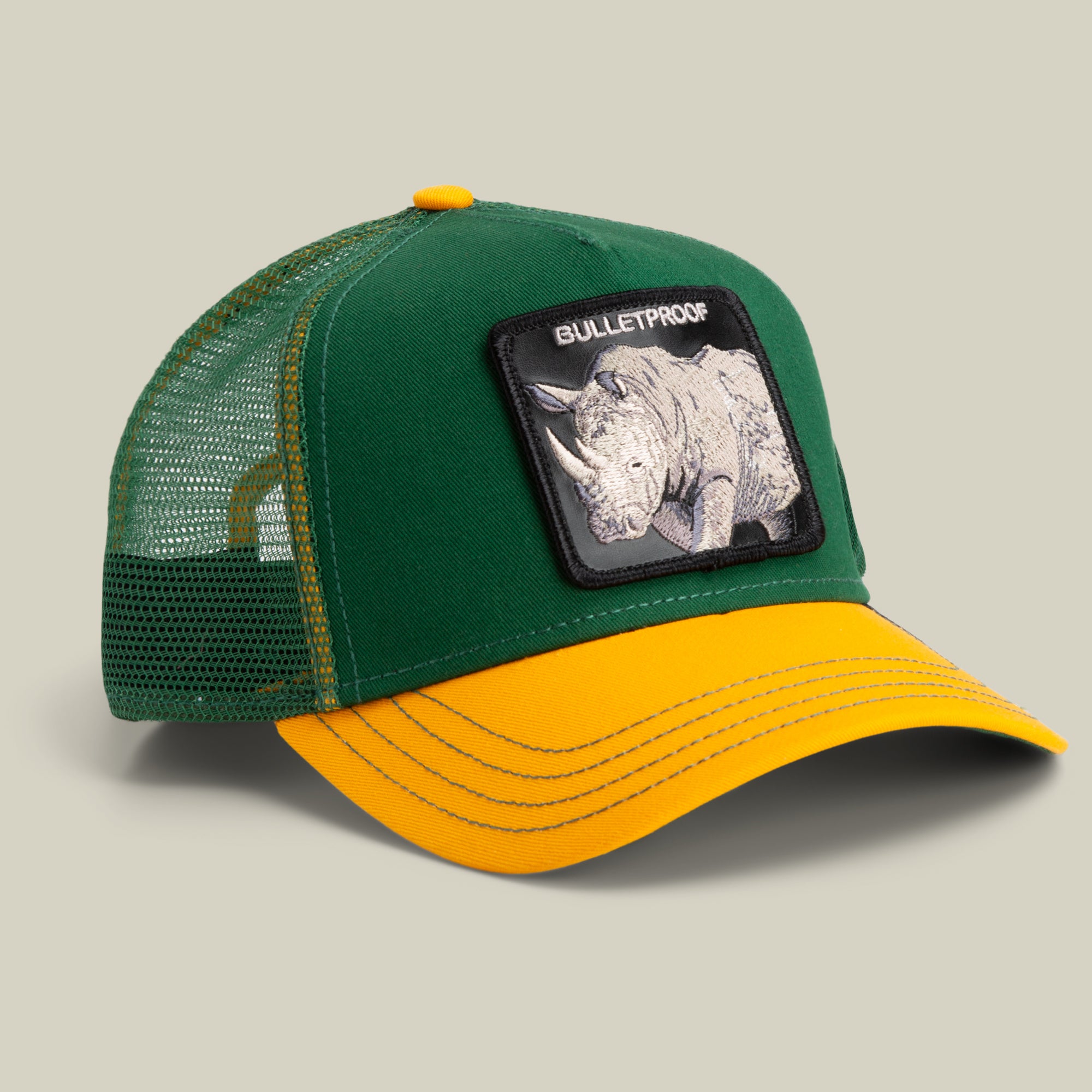 The Farm's "The Bulletproof Rhino" trucker cap features a green and yellow design, mesh back, and a rhinoceros patch labeled BULLETPROOF on the front. All sales are final.
