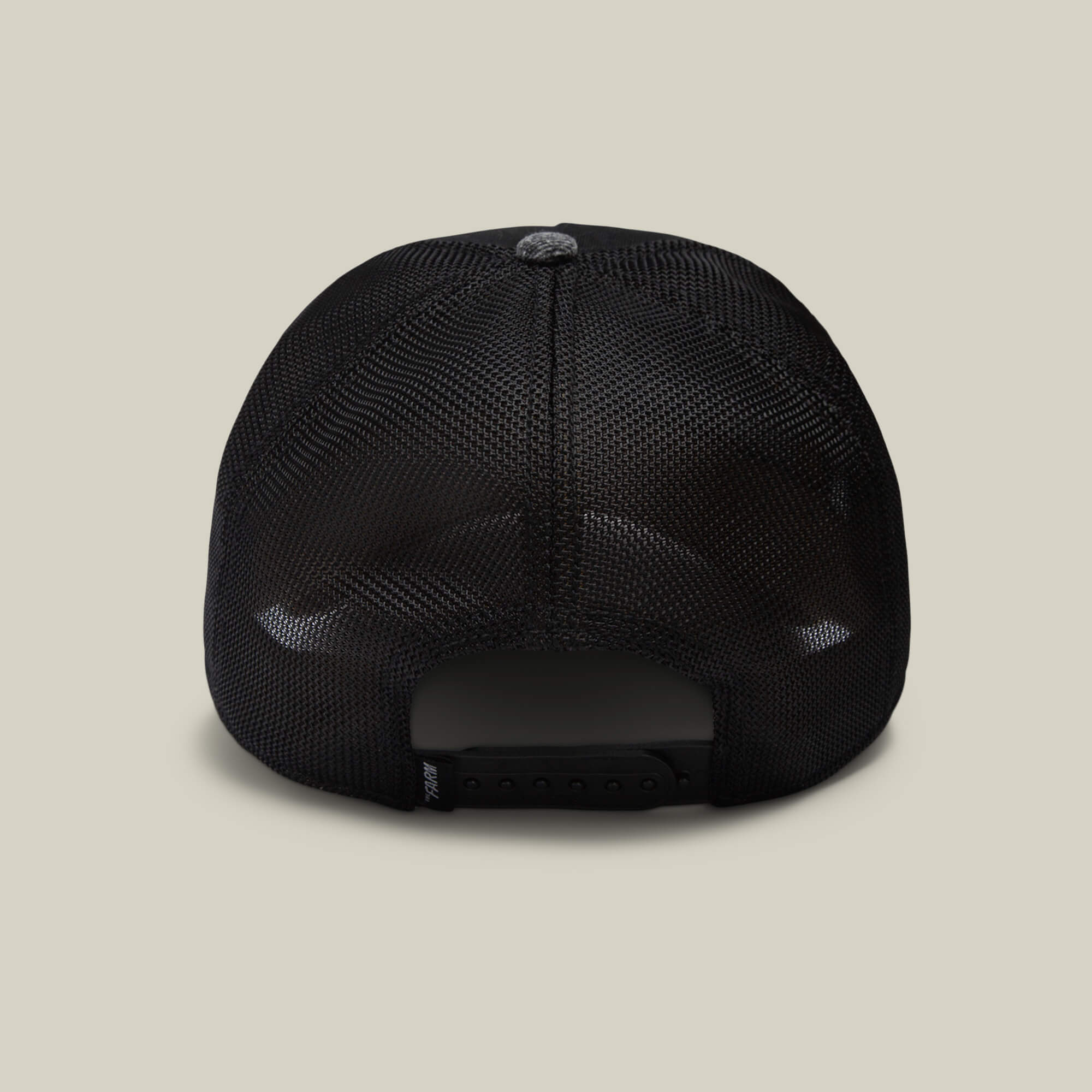 Back view of The Farm's OG Tortoise black mesh trucker hat with adjustable snapback closure, set against a beige background—pairs effortlessly with your favorite long lasting denim for a timeless style.