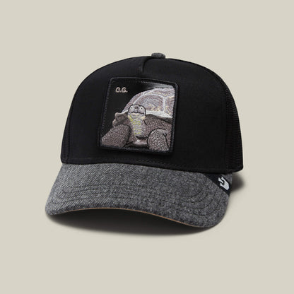 The Farm’s The OG Tortoise is a black and grey denim baseball cap with a front patch featuring an embroidered tortoise and “O.G.” above it.