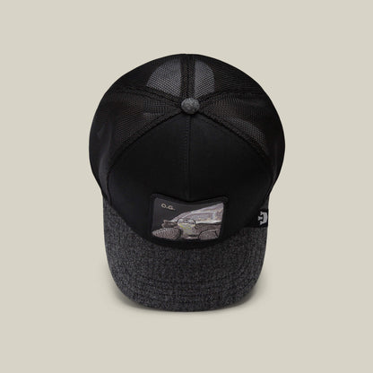 The OG Tortoise by The Farm is a black trucker cap with a textured gray brim and a front patch featuring a car illustration labeled "O.G.", perfect for pairing with your favorite long-lasting denim.