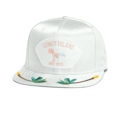 The Island Getaway by Goorin Bros. is a white flat-bill cap featuring a Coney Island NYC-1895 patch, palm tree and birds-of-paradise embroidery—ideal for your next boardwalk stroll.