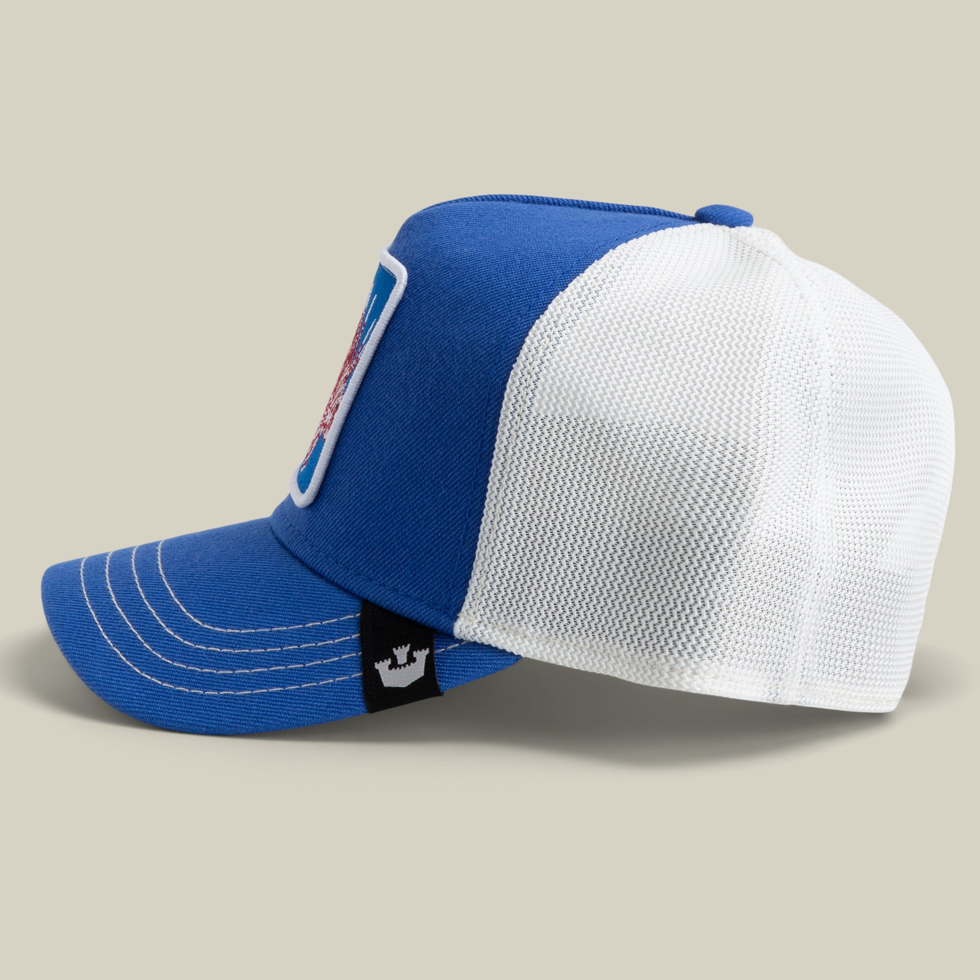 The Farm Lionfish Heat trucker hat features a blue and white design with mesh back, white stitching, a rectangular front patch, and a black side tag with crown logo. All sales final.