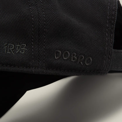 Close-up of a black Fine Headwear papa cap by Goorin Bros., featuring the word DOBRO and Chinese characters embroidered in matching black thread.