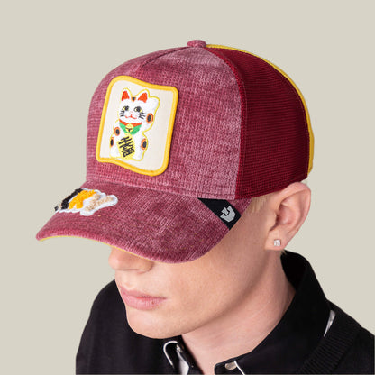 A person wears the Goorin Bros. Maneki-Neko maroon and yellow mesh cap, featuring a lucky cat patch on the front and a small embroidered cat on the visor, reminiscent of a playful LUCKY beanie, facing slightly downward.