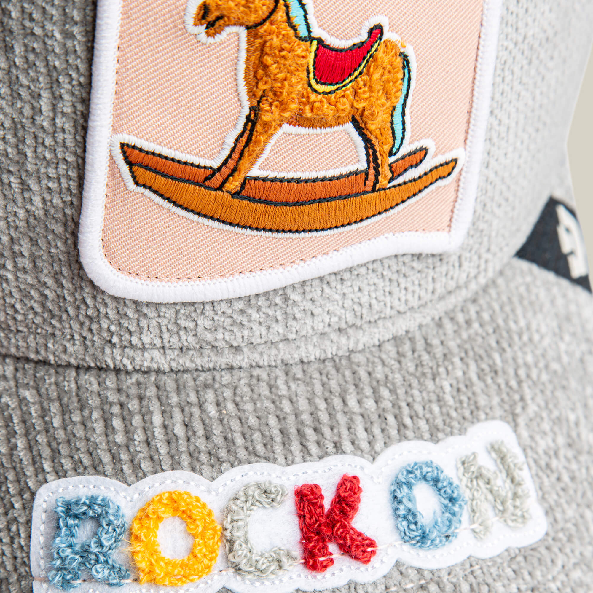 Close-up of Goorin Bros. Hobby Horse gray textured fabric with a streetwear vibe, featuring a rocking horse patch and a multicolored embroidered "ROCK ON" patch.