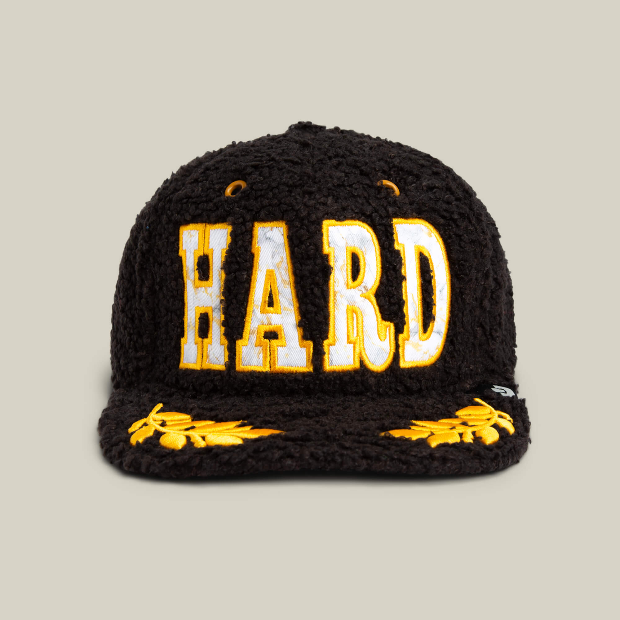 The Goorin Bros. Marble Madness cap features a black textured design, bold yellow and white "HARD" lettering on the front, gold details, and yellow embroidered leaf patterns on the brim.