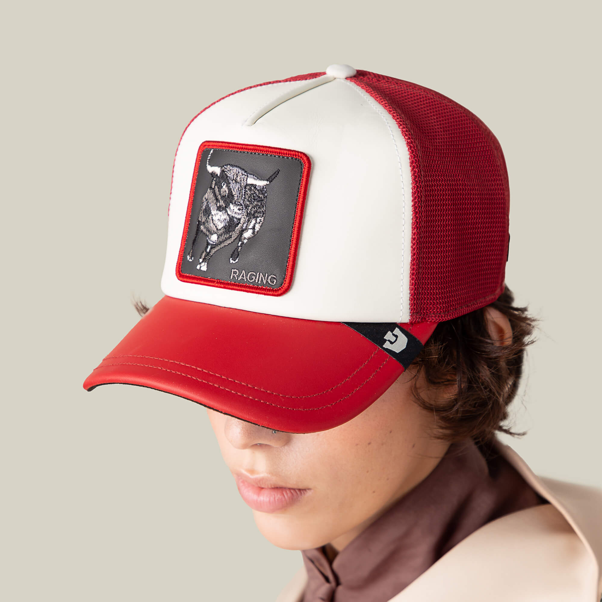 A person wearing the Goorin Bros. LFG Raging Bull trucker hat featuring a bold bull patch, the word "RAGING," and a striking red brim stands against a plain background.