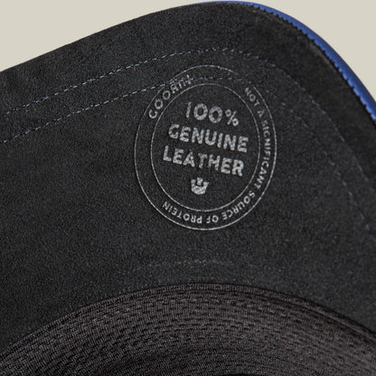 Close-up of the Goorin Bros. LFG Stallion, a black leather item with royal blue stitching and a "100% Genuine Leather - Not a Significant Source of Protein" stamp. Blue stitching lines the edge.
