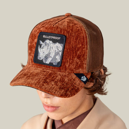 A person wearing the Iced Rhino cap by Goorin Bros.—a velvet rust hat with mesh back, featuring a BULLETPROOF patch and metallic rhino tank design.
