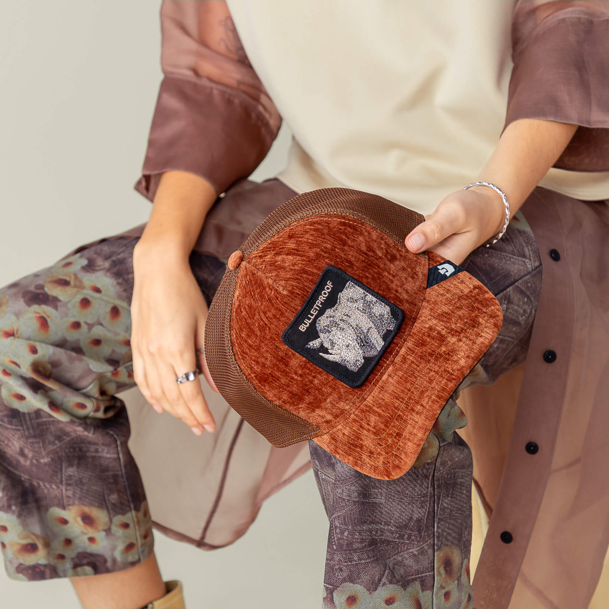 A person holds the Goorin Bros. "Iced Rhino" cap, styled with patterned pants, a sheer brown shirt, a beige top, and velvet rust accents.